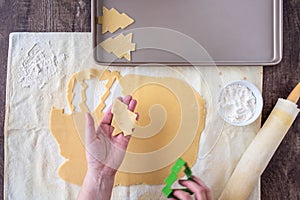 WomanÃ¢â¬â¢s hands cutting out Christmas tree sugar cookies, pastry cloth, cookie sheet